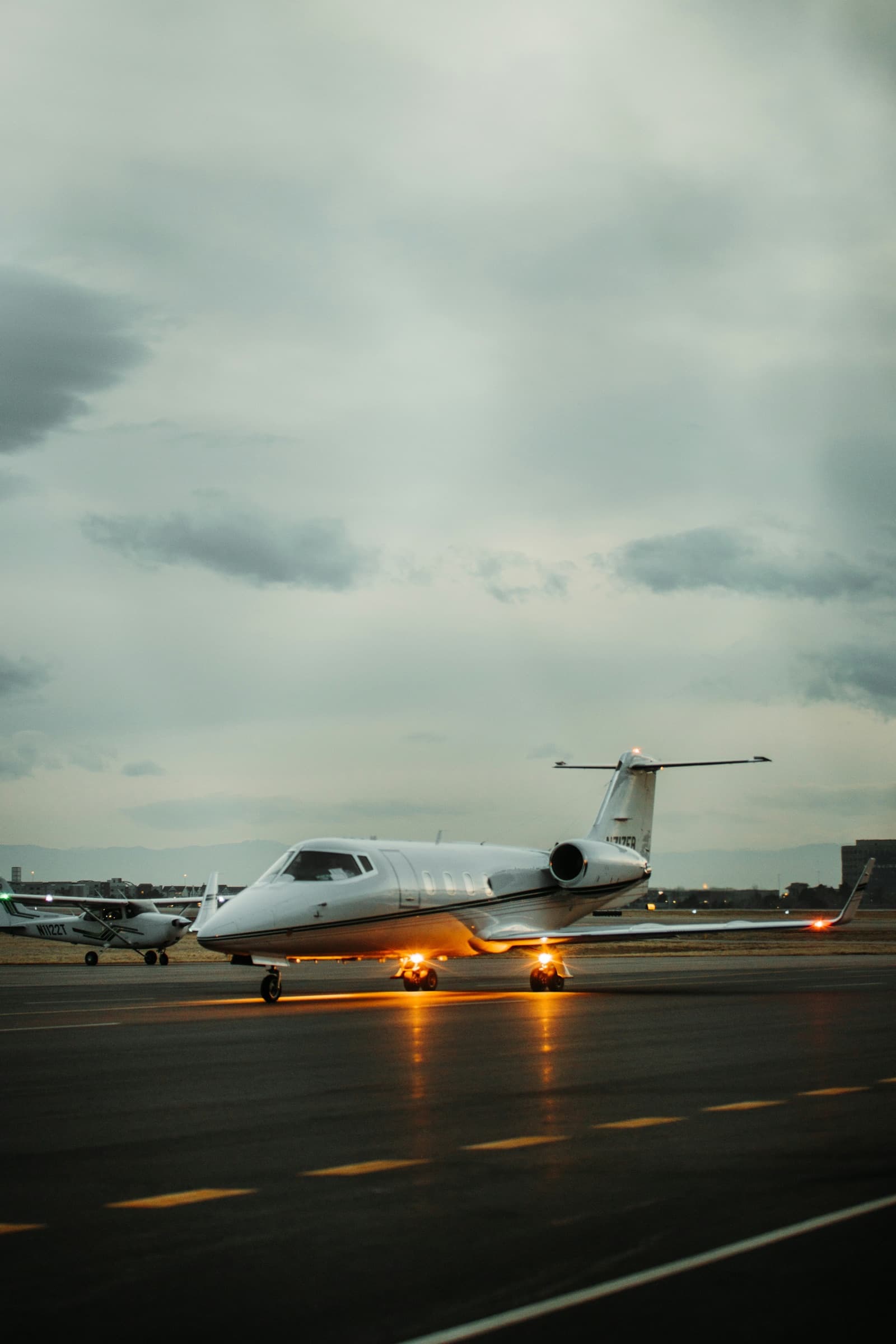 Ein Business-Jet rollt in der Dämmerung, seine Scheinwerfer spiegeln sich auf dem nassen Vorfeld.
