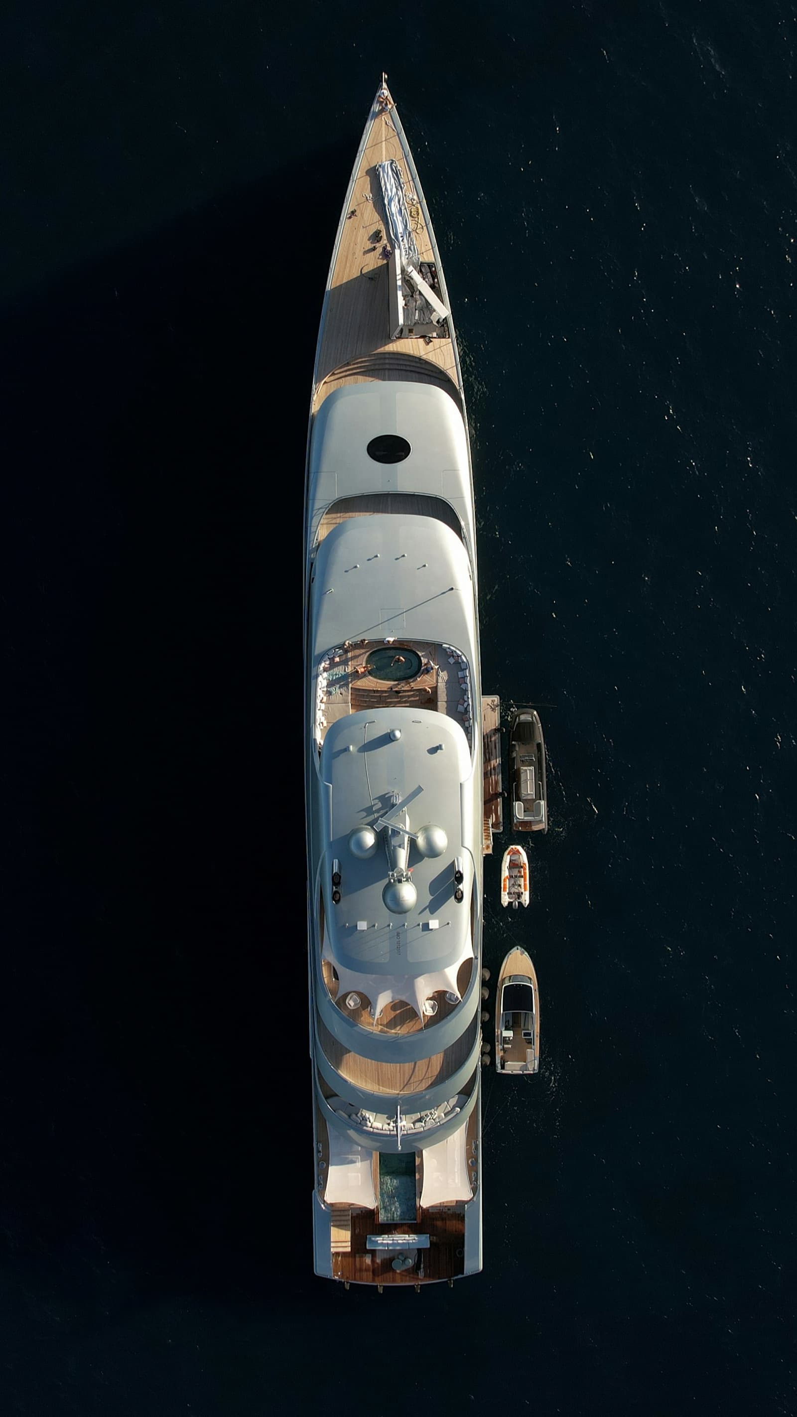 Eine Superyacht vor Anker, senkrecht von oben fotografiert, mit Beibooten längsseits auf dunklem Wasser.